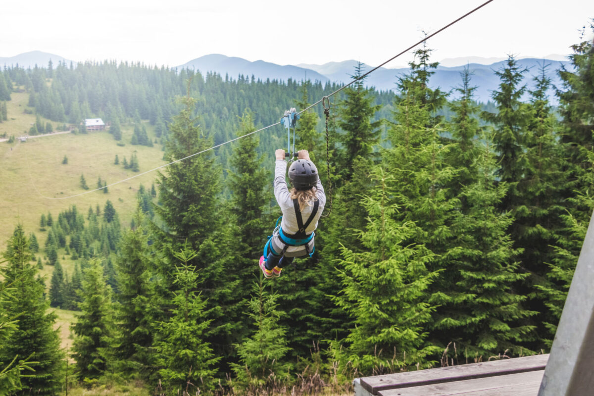 woman ziplining past tall trees with blue mountains in the distance