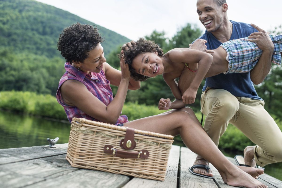 A happy family enjoying a picnic on a wooden dock by the river, surrounded by the lush ponderosa pines of the Upper Canyon, a relaxing outdoor activity for guests staying at Mountain Air Cabins in Ruidoso, New Mexico.