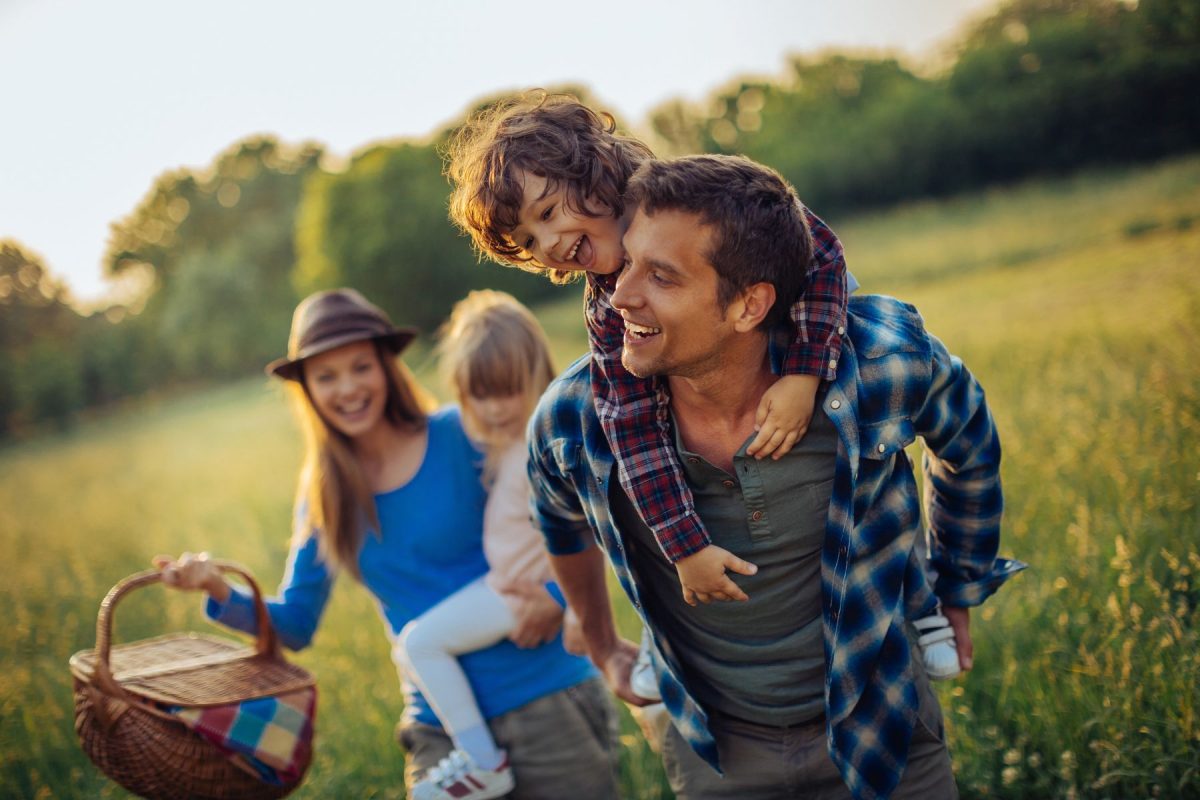 A joyful family walking through a sun-drenched meadow with a picnic basket, enjoying the crisp mountain air and scenic beauty near their Mountain Air Cabins rental in Ruidoso, New Mexico.